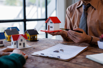 Real estate transaction with agent holding home model, investment small miniature white toy house....
