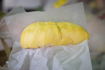 Fresh durian fruits wrapped in white paper, displayed in a market or store setting with a warm light, highlighting the distinctive yellow color and spiky texture of the fruit.