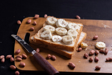 Delicious toast topped with peanut butter, banana slices,Crunchy bread slice with creamy peanut butter and sliced banana, arranged artfully on a clean chopping board with peanuts scattered arround it