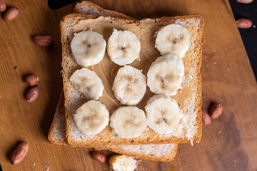 Delicious toast topped with peanut butter, banana slices,Crunchy bread slice with creamy peanut butter and sliced banana, arranged artfully on a clean chopping board with peanuts scattered arround it