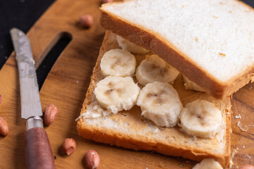 Delicious toast topped with peanut butter, banana slices,Crunchy bread slice with creamy peanut butter and sliced banana, arranged artfully on a clean chopping board with peanuts scattered arround it