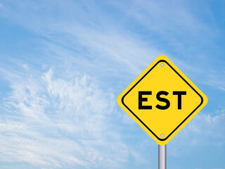 Yellow transportation sign with word EST  (abbreviation of established, estimated, eastern time zone, expressed sequence tag) on blue color sky background