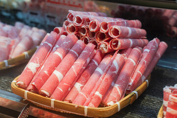 Freshly sliced rolls of beef neatly arranged on a plate, ready for hotpot or grilling.