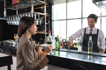 Chic female Asian office worker drinking glass of wine at counter bar after work