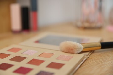 Eyeshadow palette with brush on wooden dressing table indoors, closeup. Cosmetic products