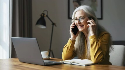 Engaging senior woman using smartphone and laptop in cozy home office lifestyle content warm environment intimate viewpoint for connection - Powered by Adobe