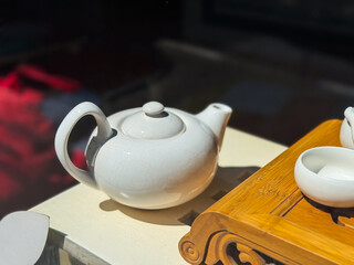 White ceramic teapot on light surface. Round teapot with curved handle and short spout next to...
