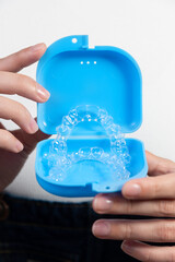Hands of a Caucasian young woman holding dental aligners and a case for them