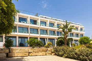 Larnaca, Cyprus, 5 May 2025, Modern Lebay Beach Hotel Exterior With Umbrellas And Pool Area. Modern Hotel Building With Balconies And Lush Greenery