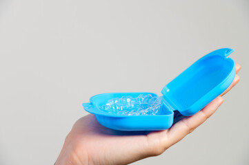 Hands of a Caucasian young woman holding dental aligners and a case for them
