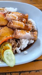 Red pork and crispy pork on rice in a blue plate on a wooden table