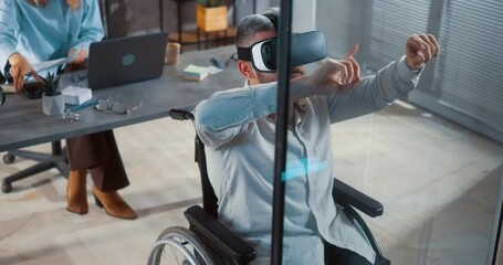 Business male worker in wheelchair using VR headset at work in office in front of glass wall, gesturing with hands in air, taking off VR glasses and looking at camera with satisfaction. - Powered by Adobe