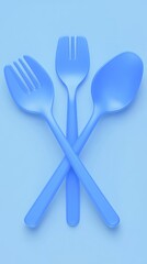Three vibrant blue plastic utensils, a fork, spoon, and serving spoon, arranged in a simple, stylized X shape against a light blue background