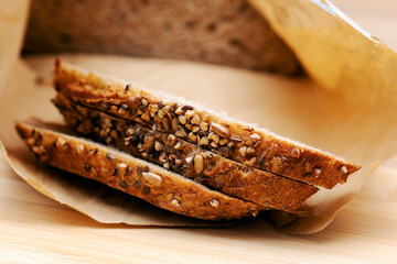 Close-up of several slices of sourdough rustic bread, generously covered with various seeds, resting on parchment paper