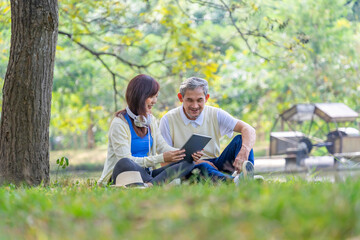bonding of young adult daughter with senior father enjoy leisure time sitting,relaxing in the park,surfing internet on tablet together