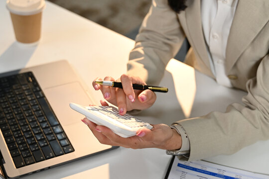 A woman is sitting at a desk with a laptop and a calculator. She is using the calculator to do some calculations
