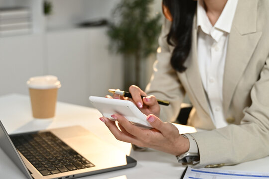 A woman is sitting at a desk with a laptop and a calculator. She is using the calculator to do some calculations