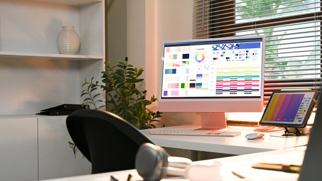 A computer monitor displays a colorful palette of colors. The room is well-lit and has a comfortable chair and a potted plant