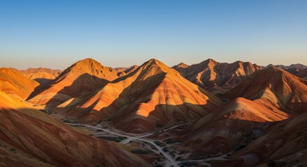 Naklejka premium Striped Hills Landscape: Majestic striped hills stand tall under a clear blue sky, bathed in the warm, golden light of either sunrise or sunset. The landscape evokes a sense of awe and wonder.