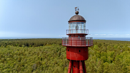 Red lighthouse stands tall above green forest on Ruhnu Island, Estonia during bright daylight