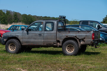 Old pickup truck parked in grassy field surrounded by other vehicles on sunny day