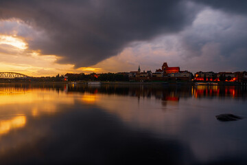  Mury miejskie, bramy i górujące nad dachami wieże kościołów tworzą  panoramę miasta.Toruń, Polska wieczorna panorama miasta nad rzeką Wisła.