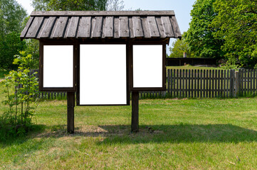 Information board stands empty in a grassy area near a wooden fence on a sunny day