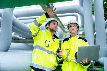 Petrochemical worker hold walkie talkie and discuss with his coworker hold laptop and stay in pipeline area in factory workplace.