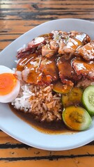Red pork and crispy pork on rice in a blue plate on a wooden  table in Thailand