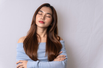 Fototapeta premium Beautiful blonde Asian woman wearing light blue off-shoulder top is tired, closed eyes and folded both hands, isolated on white background.