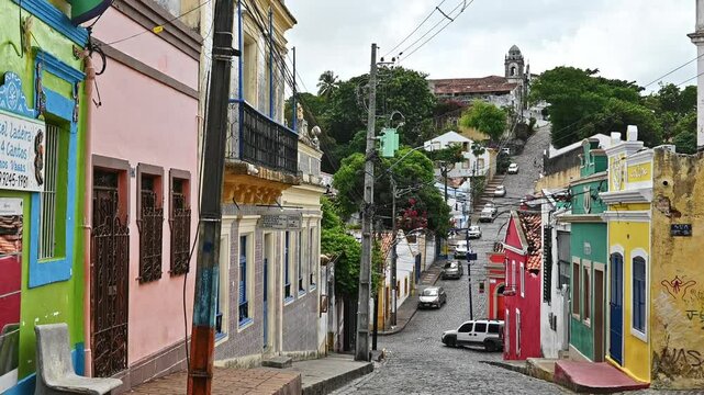 The historic city of Olinda in Pernambuco, Brazil showcasing its iconic 17th century buildings on cobblestone streets and some unidentified locals passing by.