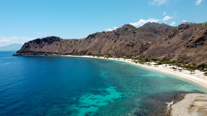 Scenic aerial view of white sand beach, turquoise ocean water, and rugged hill landscape in capital city of Dili, Timor-Leste, Southeast Asia