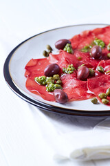Slices of beef carpaccio with olives and capers. Close up.	