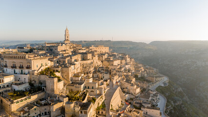 Aerial view of Matera, Italy, bathed in golden morning light. The iconic stone dwellings and cathedral tower rise above the canyon, showcasing this UNESCO-listed historic wonder