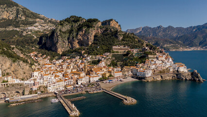 Fototapeta premium Drone view of the picturesque town of Amalfi nestled between steep cliffs and the Mediterranean Sea. A coastal gem with historic charm, sandy beach, and terraced hillsides