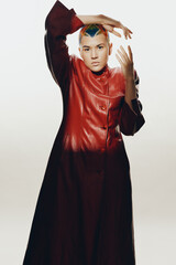 woman with colorful shaved hair in red leather coat posing with expressive hands against light...