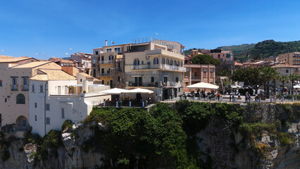 Fototapeta premium People relaxing at cafe tables overlooking scenic coastline in Tropea, Italy