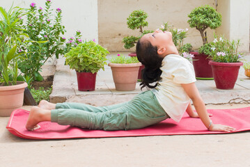 Girl going cobra pose on yoga mat, outside her home in the morning