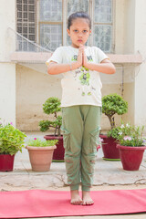 Indian pre-teen girl standing in prayer yoga pose on red mat at home garden. 