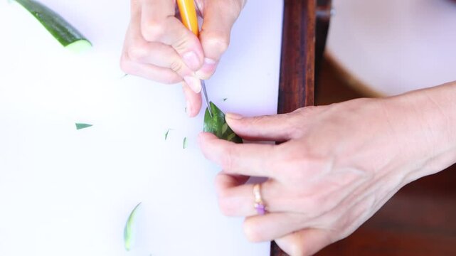 The chef is carving a cucumber with a Thai pattern using a stencil knife.