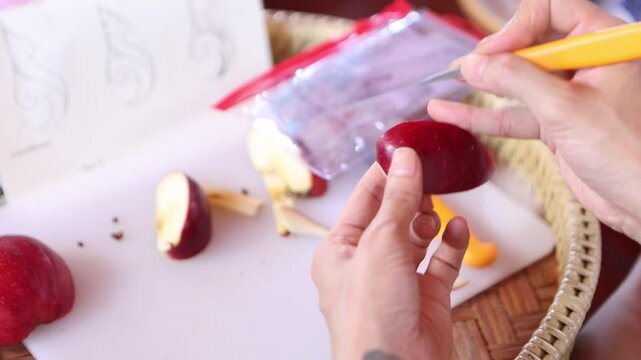 A chef is carving an apple into Thai patterns with a stencil knife.