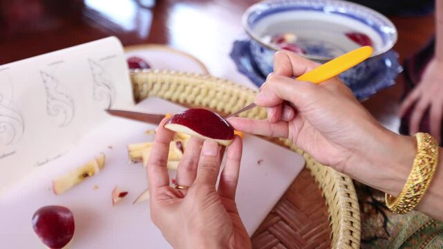 A chef is carving an apple into Thai patterns with a stencil knife.