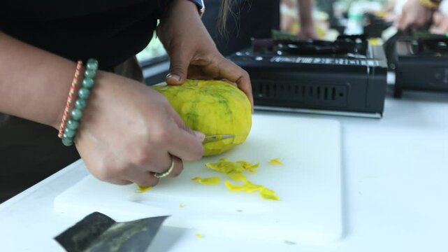 The chef is making patterns on a pumpkin using a stencil knife.