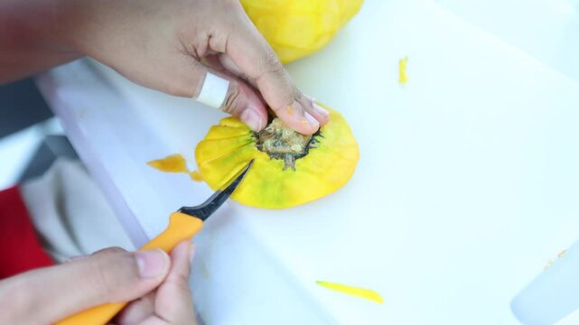 The chef is making patterns on a pumpkin using a stencil knife.