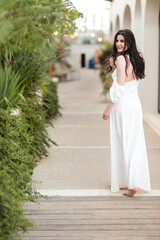 Beautiful young girl with long dark hair in a white long dress in summer