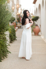 Beautiful young girl with long dark hair in a white long dress in summer