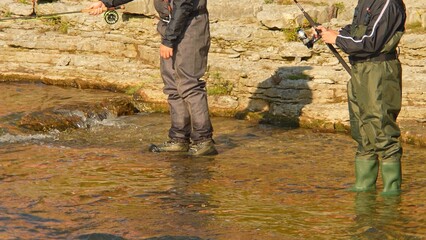 Unrecognizable fisherman fly fishing. Angler fly fishing at the river and casts the line. Close up of fly rod and reel at sunny day with rocks in the background.