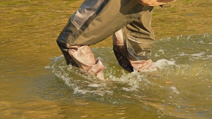 Unrecognizable Fisherman or Angler walks in the wader and wading boots at the slippery rocky rapid river or creek for the salmon and trout spot to fish. Fishing game and sport for fisherman.