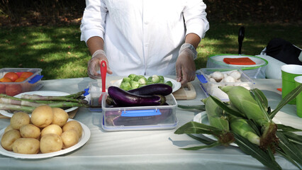 Garden picnic party celebration preparation. Seasoning Brussels sprouts, cabbage vegetables for BBQ grill cooking. Women chef in white short brushing oil on BBQ food to grill outdoors.