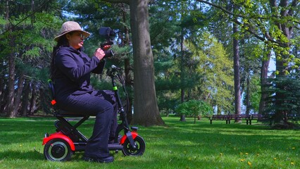 A female videographer person with physical disabilityusing and riding a three wheel wheelchair or e scooter for video recording and content creating. Freedom and independence concept.
